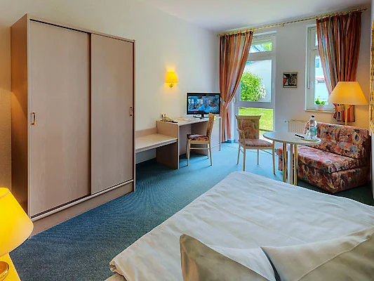Einzelzimmer mit Bett, Schreibtisch, Sitzecke und Fenster zum Garten