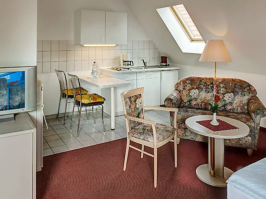 Komfortzimmer mit weißer Küchenzeile, Essplatz unter dem Dachfenster und Sofa
